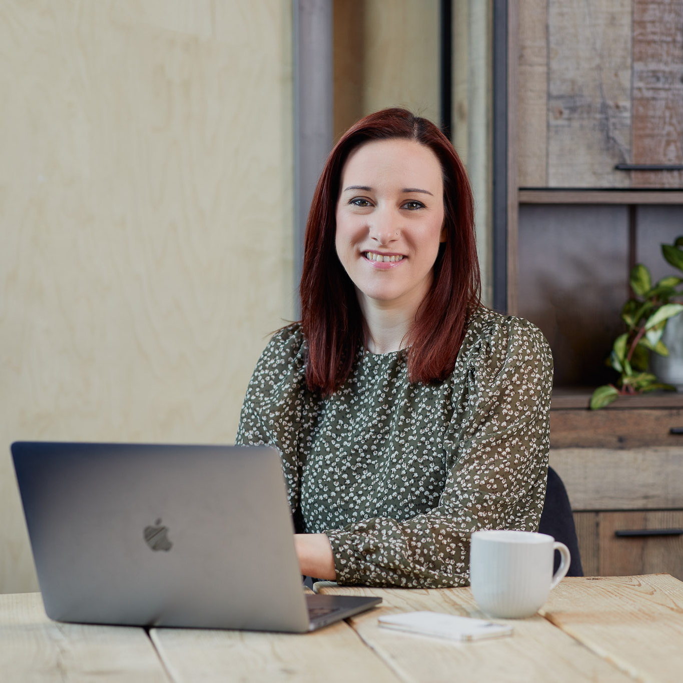 Woman in green top, with a laptop and mug on a wooden desk